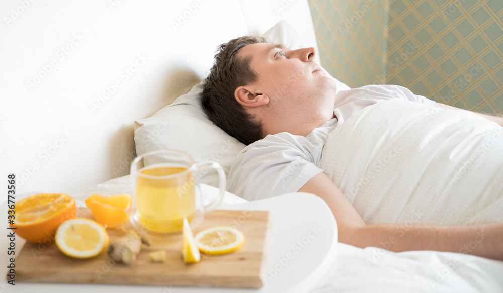 Cup with antipyretic drugs for colds,flu.Sick man in bed. Tea with citrus vitamin C,ginger root,lemon,orange.Wooden tray. Home self-treatment.Medical quarantine antiviral covid-19 coronavirus therapy