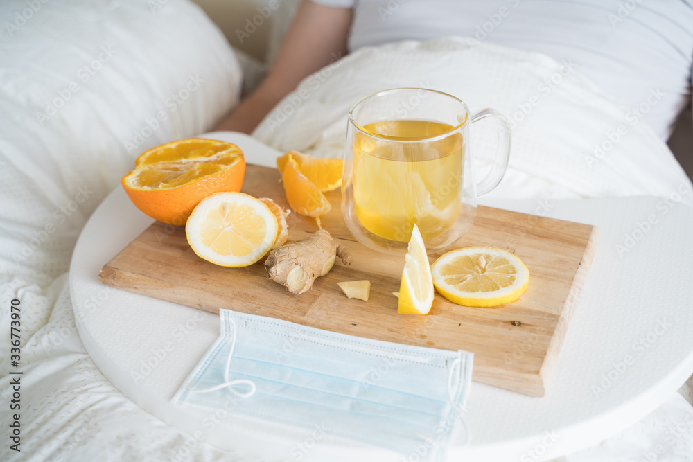 Cup with antipyretic drugs for colds,flu.Sick man in bed. Tea with citrus vitamin C,ginger root,lemon,orange.Wooden tray. Home self-treatment.Medical quarantine antiviral covid-19 coronavirus therapy Cup with antipyretic drugs for colds,flu.Sick man in bed. Tea with citrus vitamin C,ginger root,lemon,orange.Wooden tray. Home self-treatment.Medical quarantine antiviral covid-19 coronavirus therapy