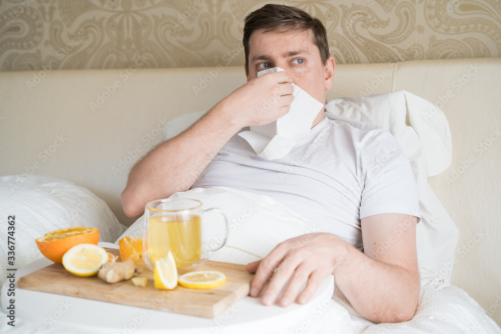 Cup with antipyretic drugs for colds,flu.Sick man in bed. Tea with citrus vitamin C,ginger root,lemon,orange.Wooden tray. Home self-treatment.Medical quarantine antiviral covid-19 coronavirus therapy