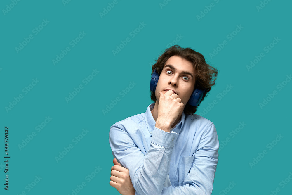Portrait of a young beautiful man wearing white t-shirt and blue shirt in headphones over blue background Portrait of a young beautiful man wearing white t-shirt and blue shirt in headphones over blue background