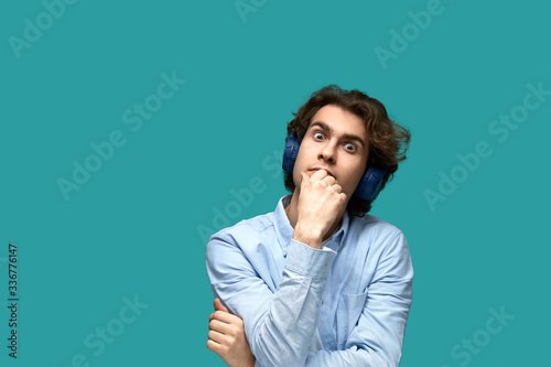 Portrait of a young beautiful man wearing white t-shirt and blue shirt in headphones over blue background
