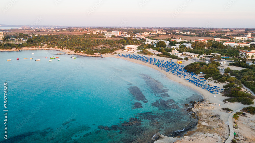 Aerial bird's eye view of Landa beach, Ayia Napa, Famagusta, Cyprus. Landmark tourist attraction golden sand bay at sunrise with boats anchored between Makronissos and nissi in Agia Napa, from above. 