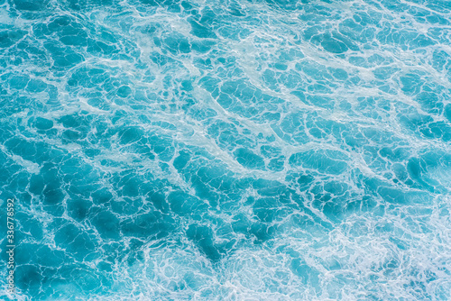 The azure surface of the ocean. Waves break at the shore. Texture of the water surface near the shore above the coral reef. Aerial photography of water.