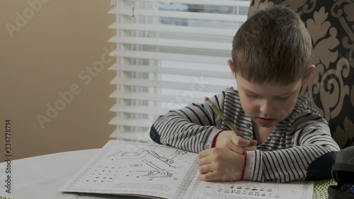 little diligent boy studying his homework at home he sits at a table and draws in coloring. child is focused on drawing a preschooler enjoying his activity. happy childhood