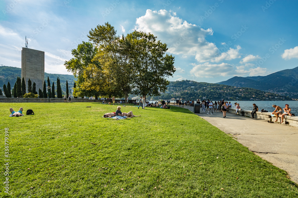 Como, ITALY - August 4, 2019: Local people and tourists on the promenade along the lake in the center of beautiful Italian Como city. Warm sunny summer day in very popular holiday destination. Como, ITALY - August 4, 2019: Local people and tourists on the promenade along the lake in the center of beautiful Italian Como city. Warm sunny summer day in very popular holiday destination.