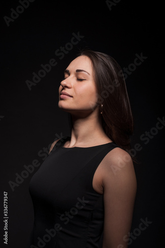 Gentle young satisfied lady with closed eyes in the darkness. Elegant black dress, so dark everywhere. Amazing girl with attractive appearance