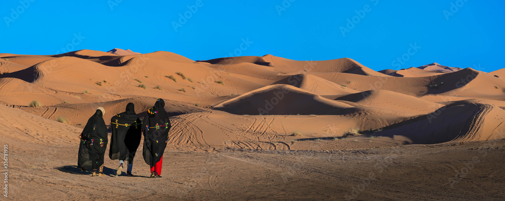 Fototapeta premium Drei Frauen gehen über die Sanddünen in Erg Chebbi Marokko, Panorama 