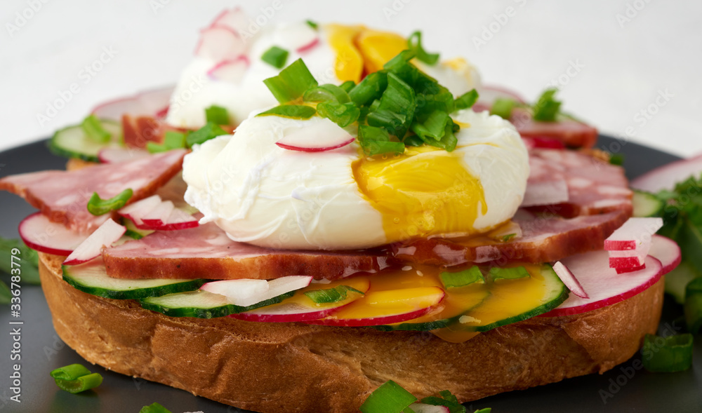 sandwich on toasted white slice of bread with poached eggs, green leaves of arugula, cucumber and radish, morning breakfast on a round plate sandwich on toasted white slice of bread with poached eggs, green leaves of arugula, cucumber and radish, morning breakfast on a round plate