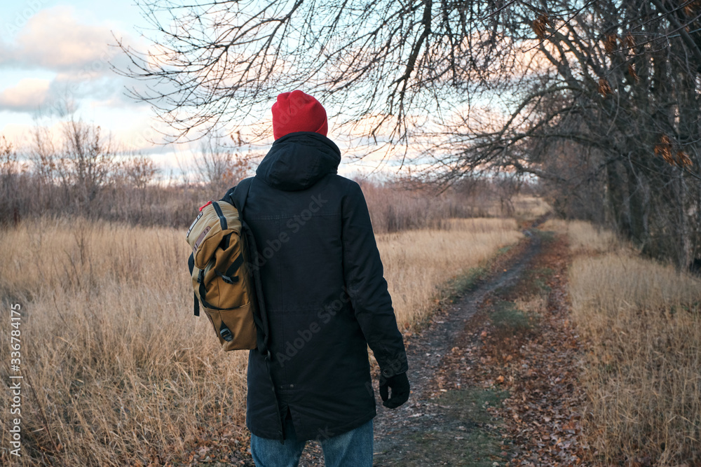 A man walking in a field outdoors. Beautiful autumn landscape, fall foliage. Rural scenic sunset. Rest and recovery in the weekend. Stylish man with backpack in casual clothes. Evening adventure A man walking in a field outdoors. Beautiful autumn landscape, fall foliage. Rural scenic sunset. Rest and recovery in the weekend. Stylish man with backpack in casual clothes. Evening adventure