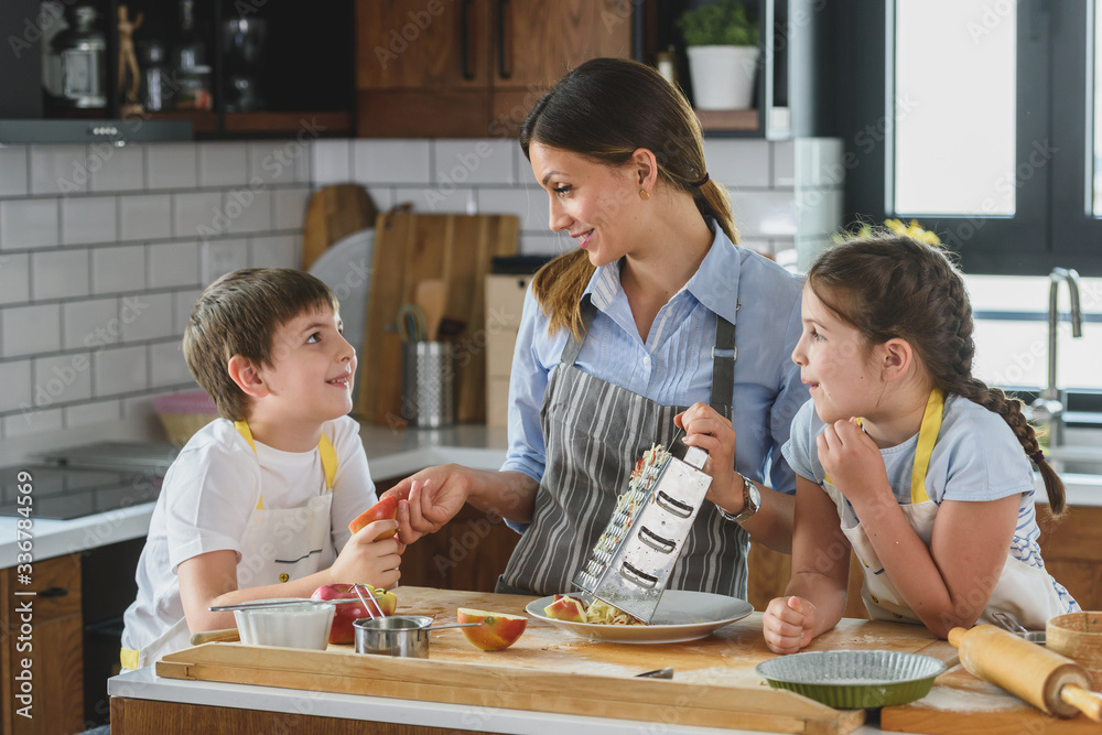 Mother and her kids making apple pie in the kitchen. Teaching children to help at home Mother and her kids making apple pie in the kitchen. Teaching children to help at home
