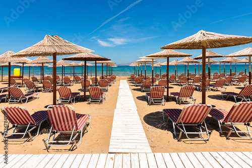 Empty beach with chairs  sunbeds  straw umbrellas  and blue sky. Mediterranean summer vacation destination  Heraklion  Crete  Greece.