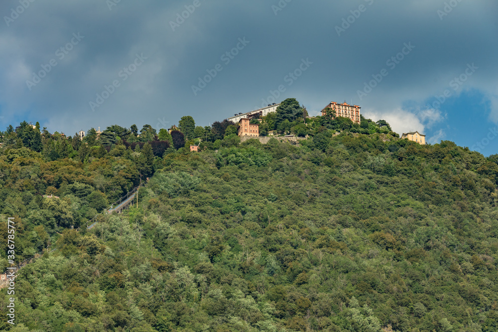 Obraz premium Como, ITALY - August 4, 2019: Apartments, villas, hotels on the green forested mountainsides near Lake Como. Beautiful Italian Como city. Warm sunny summer day in very popular holiday destination