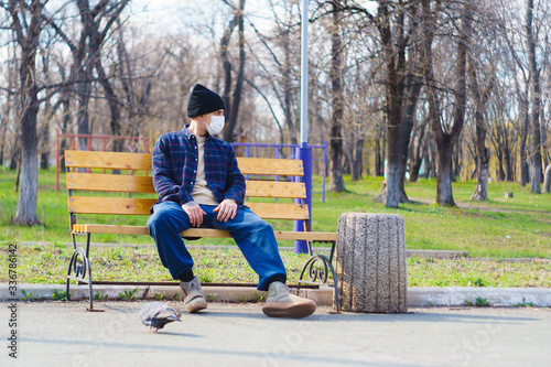 medical mask as protection against coronavirus. guy sits alone on a bench