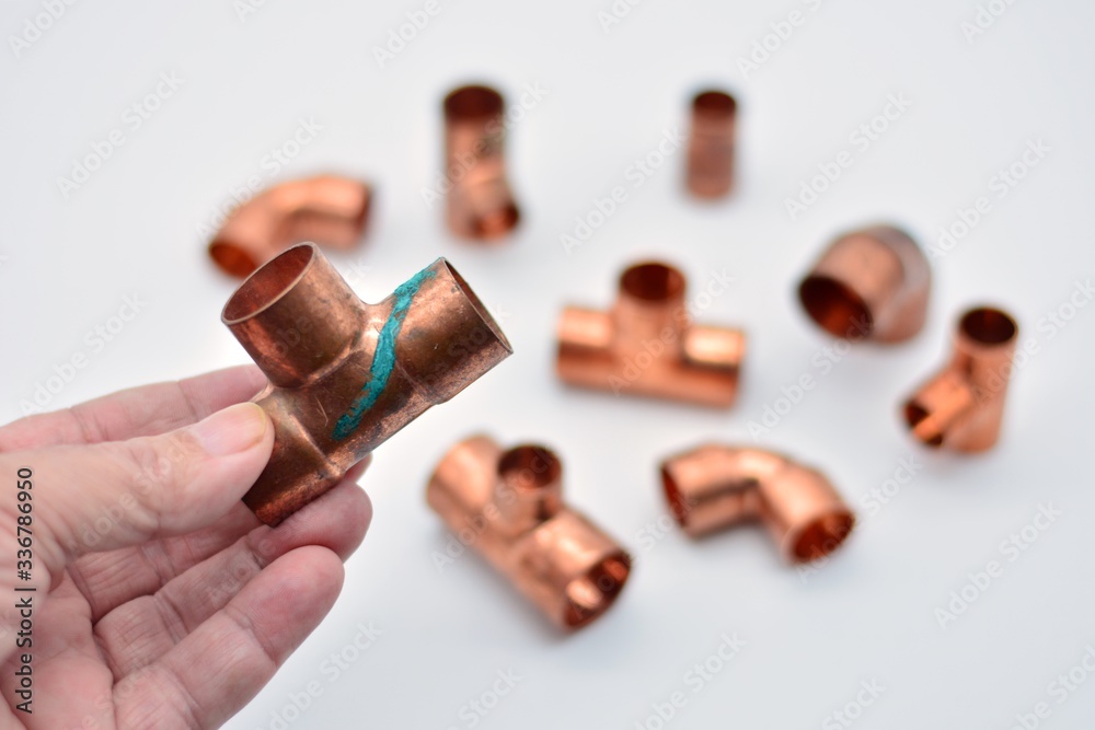 Piezas de cobre para agua, destacando una te con óxido de cobre	en la mano