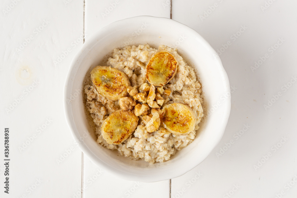 Oatmeal porridge in a bowl with baked bananas, honey and nuts. Healthy vegetarian or vegan breakfast. Copy space, top view. 