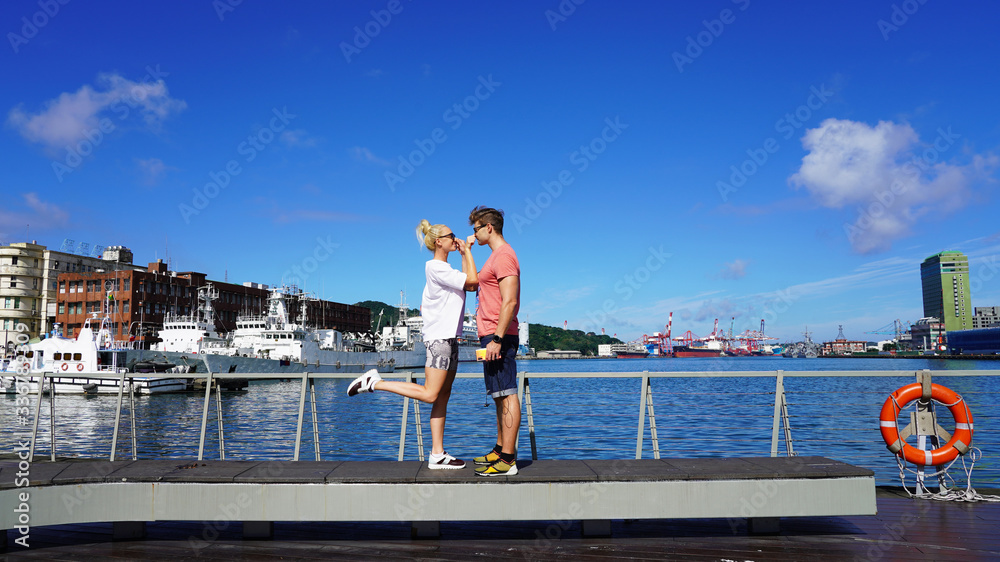 Pretty young European couple, handsome guy and beautiful girl on sunny day have a rest on the embankment in port against the background of ships and boats. emotions joy love happiness. relationship