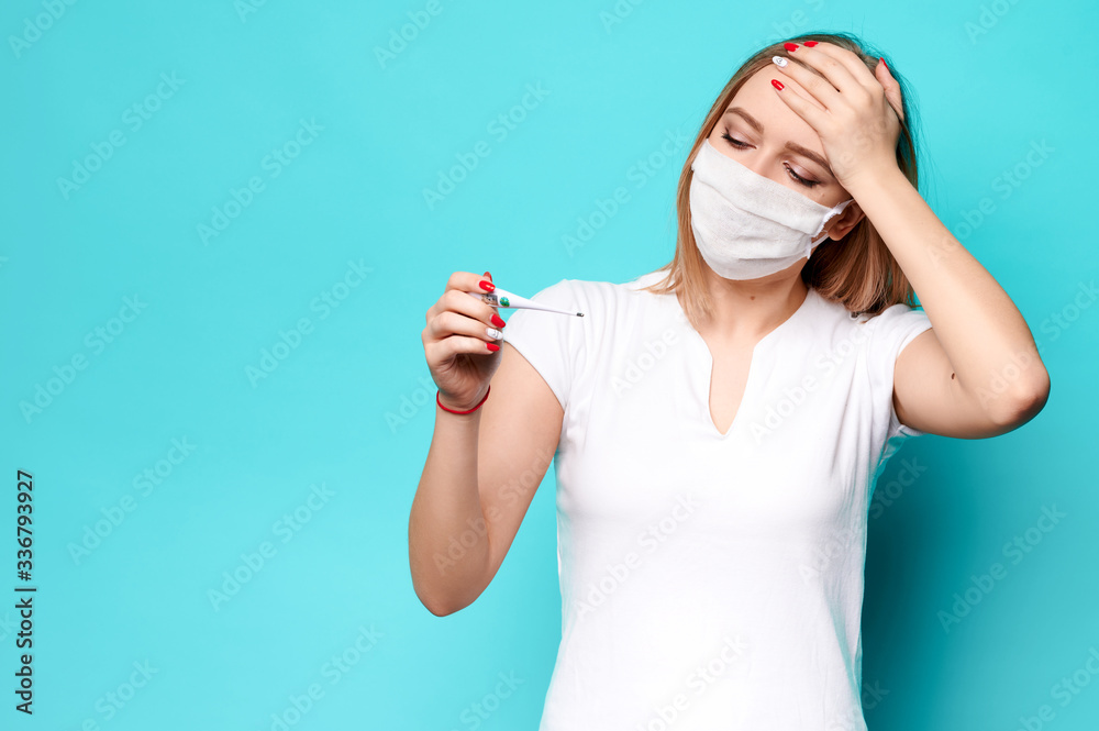 Young woman in a protective mask on an isolated background measures the temperature with a thermometer