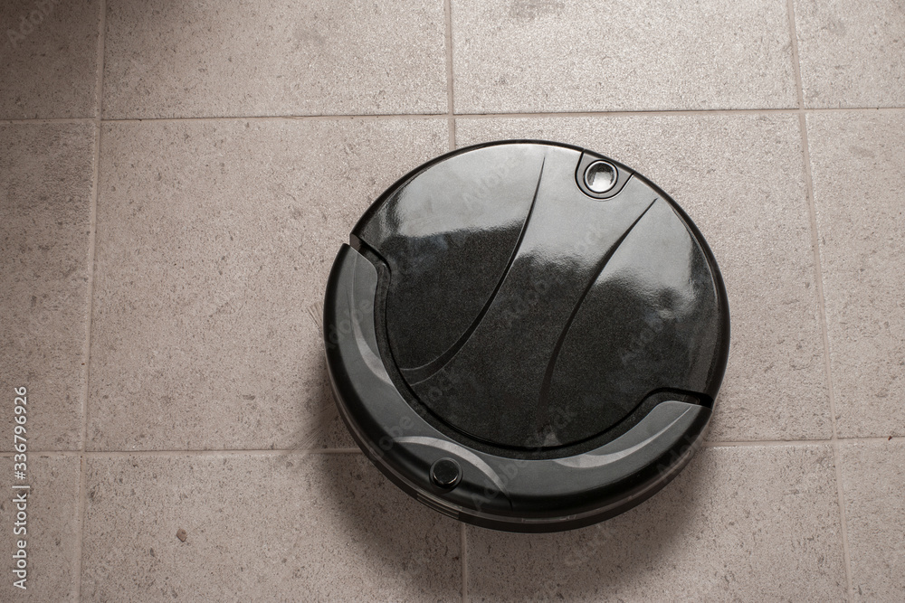 black robotic vacuum cleaner runs on tile floor. The robot is controlled by voice commands for