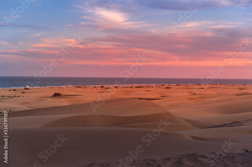 People passing through sand dunes overlooking the ocean on the horizon during a sunny day with thick clouds moving in the sky from the Grand Canary Island