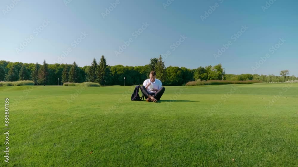 Businessman is eating his vegetarian lunch with eco-friendly packaging. Man sits in a park on green grass and eats a salad with tomatoes, cucumbers and lettuce in a paper package with a wooden fork Businessman is eating his vegetarian lunch with eco-friendly packaging. Man sits in a park on green grass and eats a salad with tomatoes, cucumbers and lettuce in a paper package with a wooden fork