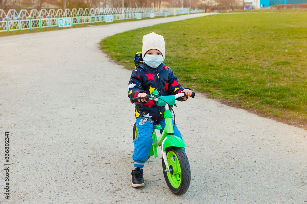 a child rides a bicycle on the street using all precautions to prevent coronavirus infection. a child rides a bicycle on the street using all precautions to prevent coronavirus infection.
