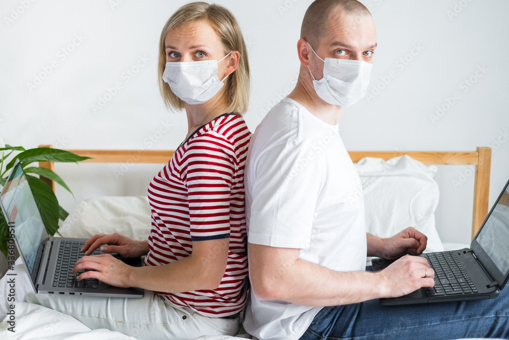 family working remotely from home siting back to back on bed. Quarantined couple coronavirus in medical masks .Stay home safe. Distance learning, education and work. Order food products online. family working remotely from home siting back to back on bed. Quarantined couple coronavirus in medical masks .Stay home safe. Distance learning, education and work. Order food products online.
