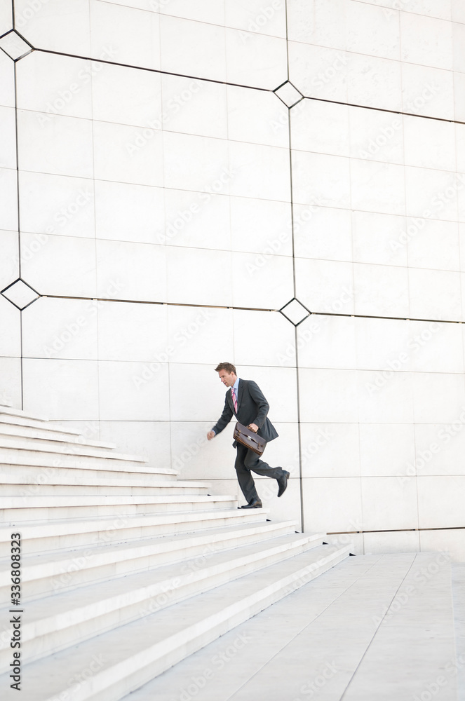 Distant businessman running outdoors up a long white staircase