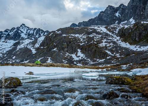 Green tent over a waterfall coming from a partially frozen lake in the wilderness of Alaska.