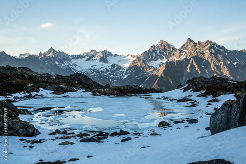 Frozen alpine lake and sunset on distant peaks in the Talkeetna Mountains in July.