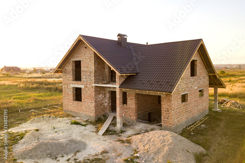 Unfinished brick house with wooden roof structure covered with metal tile sheets under construction.