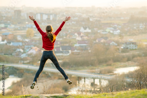 Young woman jumping with outstretched arms and legs outdoors on a distant city background. Relaxing, freedom and wellness concept.