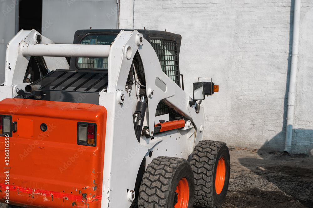 White skid steer loader at a construction site waiting of work. Industrial machinery. Industry. White skid steer loader at a construction site waiting of work. Industrial machinery. Industry.