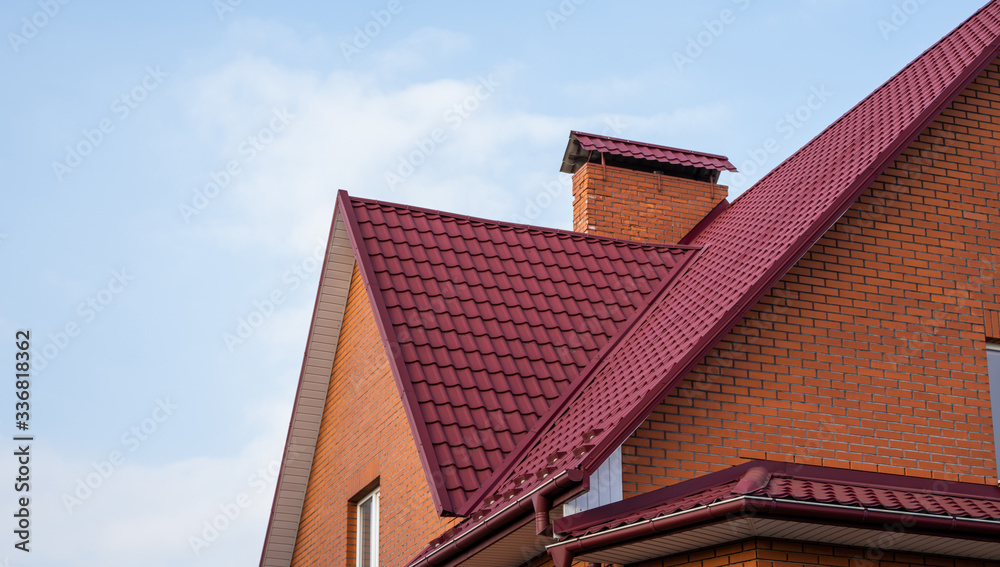 Red metal tile roof. Roof metal sheets. Modern types of roofing materials. Roof of the house, metal roof tile against the blue sky. Building.