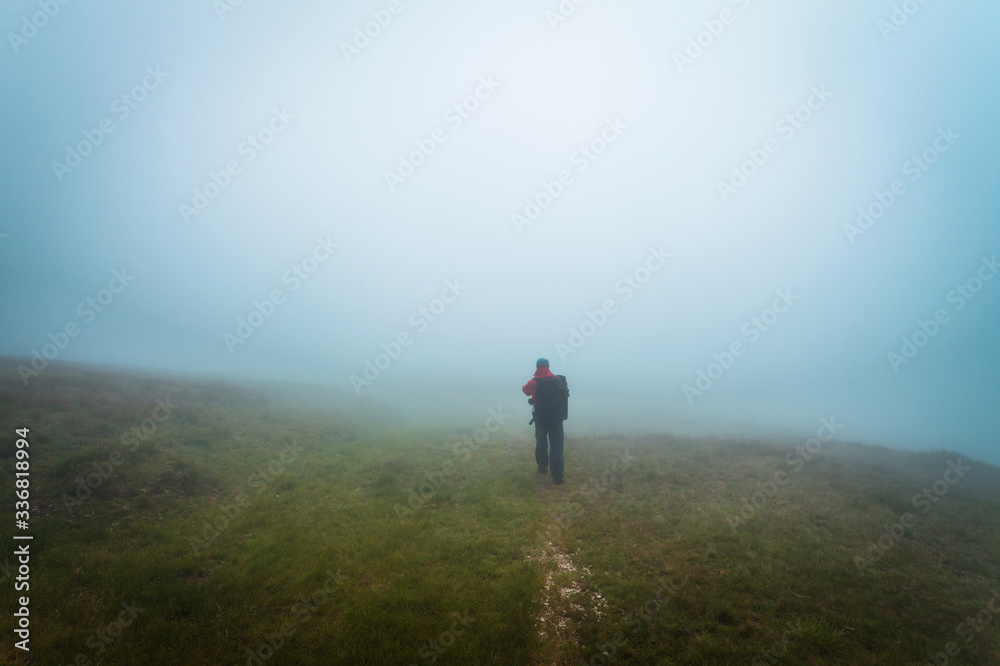 Hiker or tourist on a mountain path during foggy weather condition, risk of getting lost, danger concept