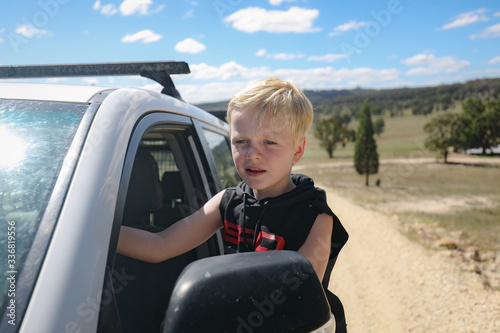 Young boy riding on outside of vehicle travelling on country road