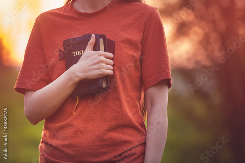 Fotografia, Obraz Girl holding a Bible tight as it is the only hope, beautiful warm color palette