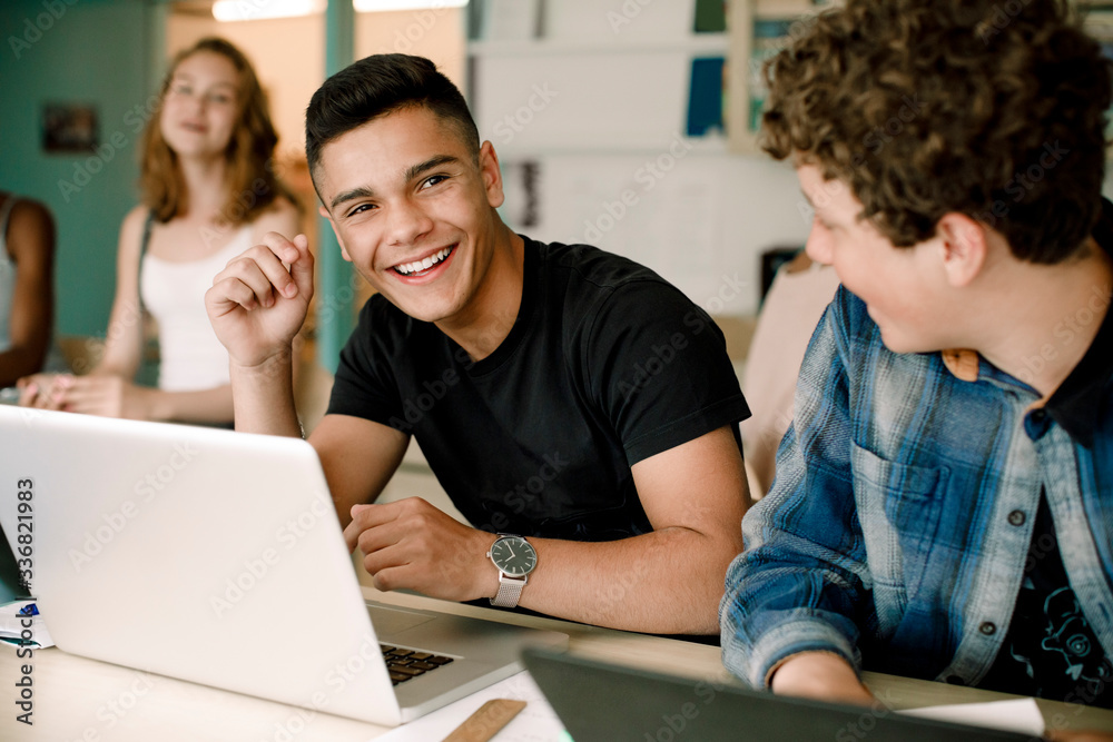 Smiling male students using laptop over table while sitting in classroom Smiling male students using laptop over table while sitting in classroom