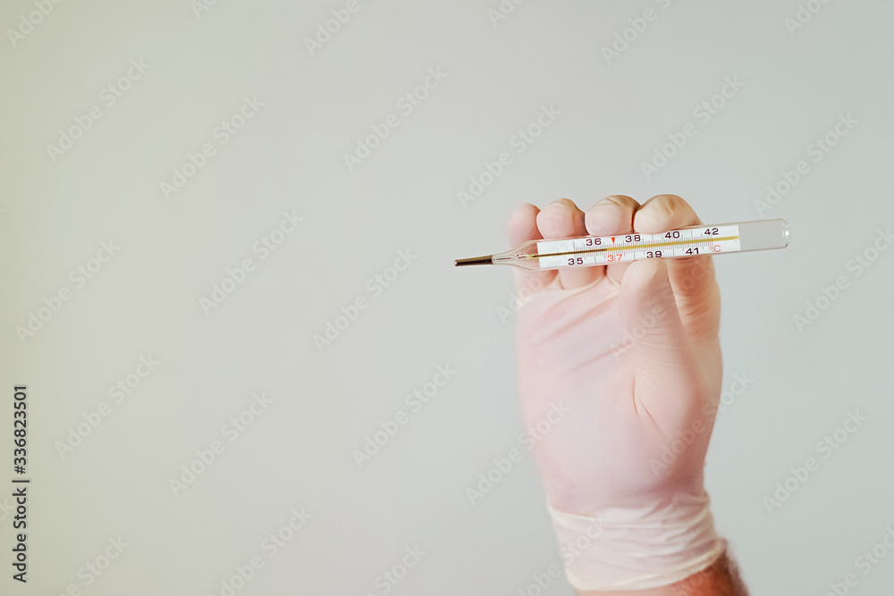 Hand in medical gloves holds a thermometer. Close-up