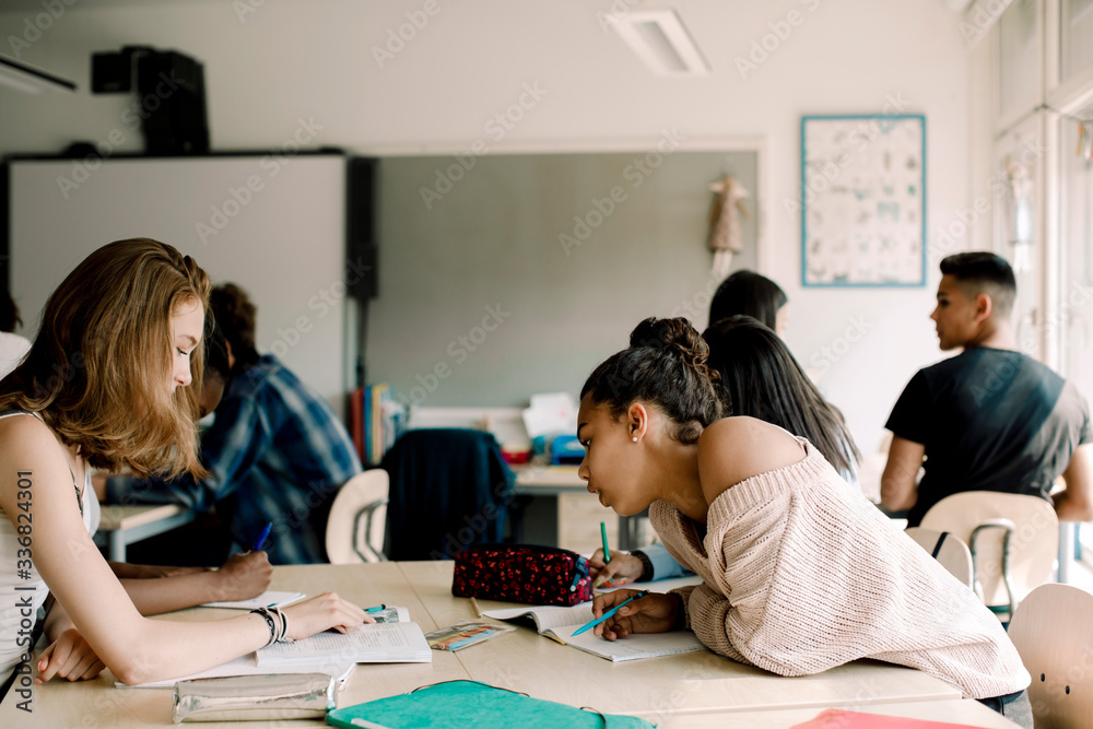 Teenage students discussing over book in classroom Teenage students discussing over book in classroom