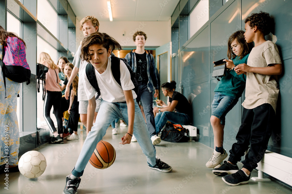 Boy playing with basketball during lunch break in school corridor Stock