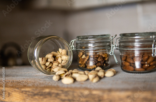 Pistachios scattered on the white vintage table from a jar and with other nuts on background. Pistachio is a healthy vegetarian protein nutritious food. Pistachios on rustic old wood.