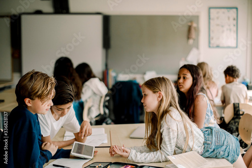 Female student leaning over table while friends sitting in classroom photo