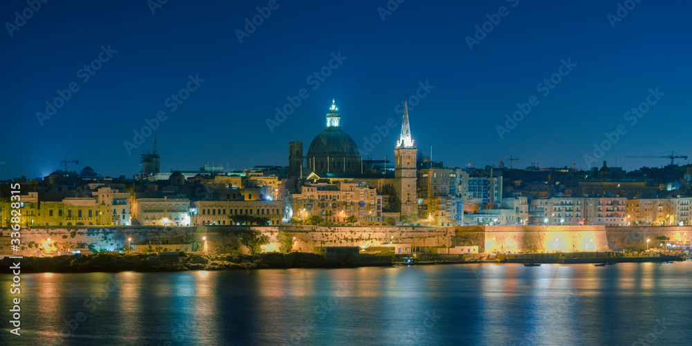 Malta's capital city Valletta, at night, from across the port in Sliema, with churches and buildings illuminated