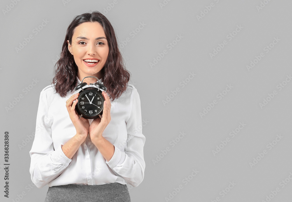 Businesswoman with alarm clock on grey background. Time management concept