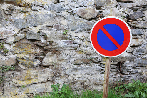 Panneau de signalisation routière devant un mur en pierre le long d'une route : interdiction de stationner.