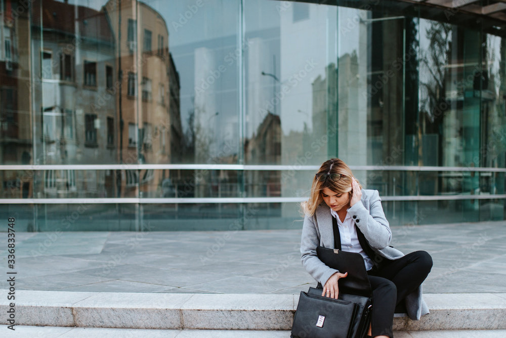 A young attractive businesswoman with a bag is sitting on the stairs in front of the company A young attractive businesswoman with a bag is sitting on the stairs in front of the company