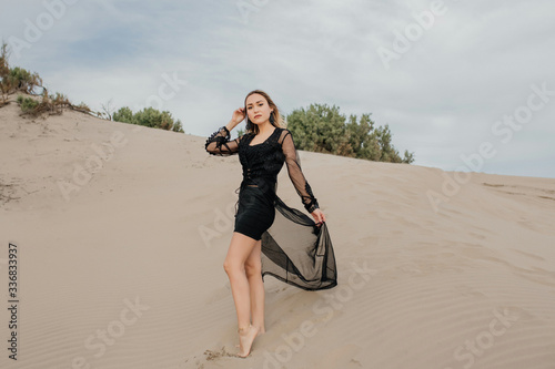 Foto de Mujer elegante parada sobre la arena con vestido negro en la playa  do Stock