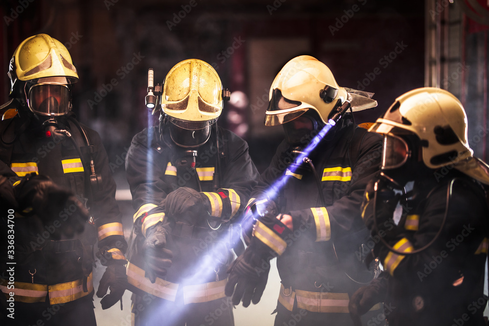 Group of professional firefighters. Firemen wearing uniforms, protective helmets and oxygen masks. Smoke in the background.
