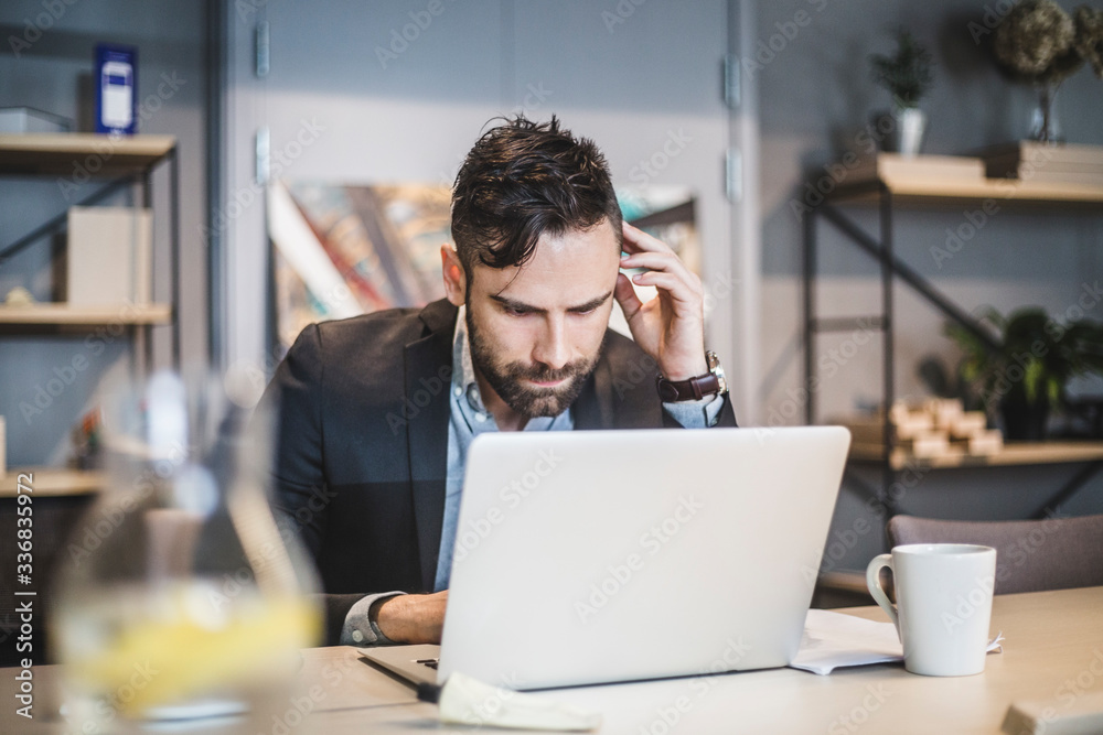 Young businessman working over laptop while sitting at table in office Young businessman working over laptop while sitting at table in office