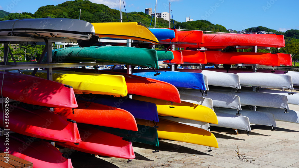 multi-colored canoes and kayaks on racks texture of colored kayaks on the background of the club's yachts on a sunny day. multi-colored canoes and kayaks on racks texture of colored kayaks on the background of the club's yachts on a sunny day.